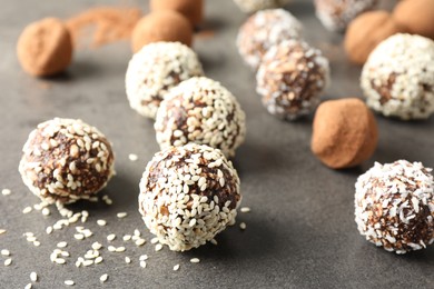 Photo of Tasty chocolate candies with cocoa powder, nuts, coconut flakes and sesame seeds on grey table, closeup