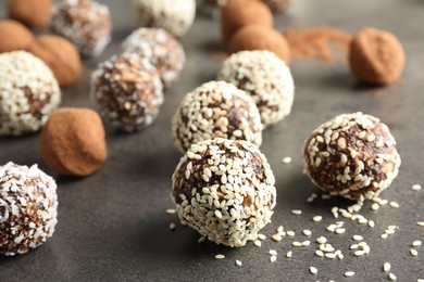 Photo of Tasty chocolate candies with cocoa powder, nuts, coconut flakes and sesame seeds on grey table, closeup