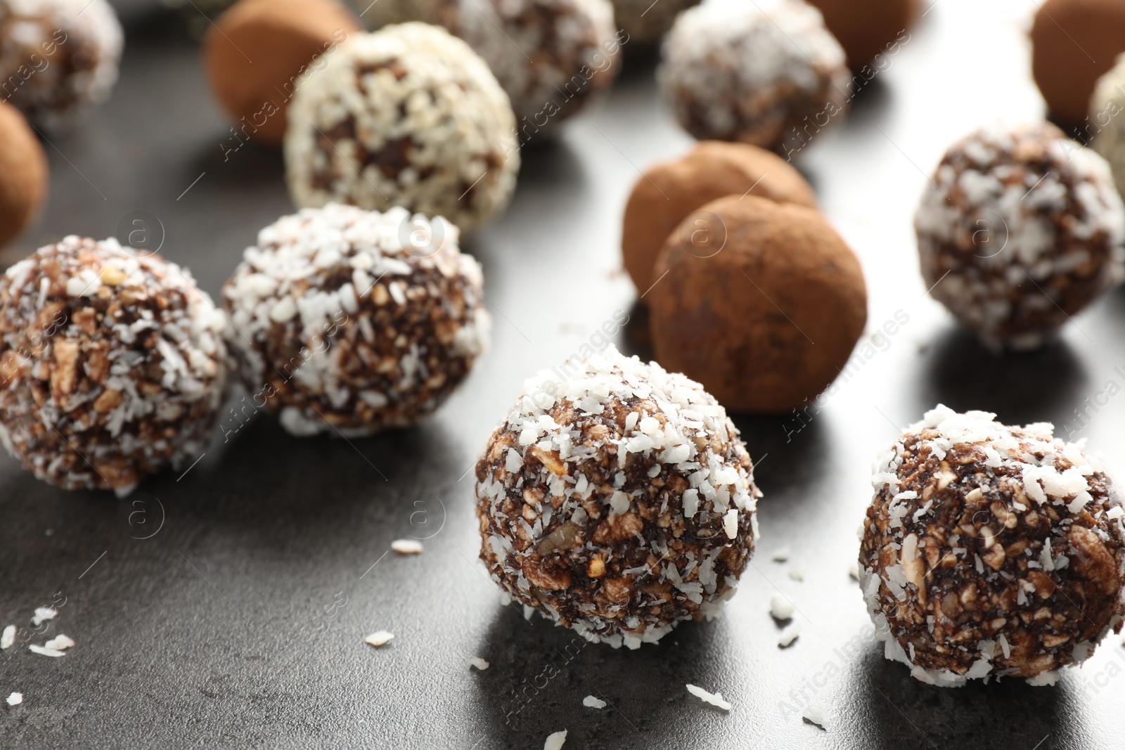 Tasty chocolate candies with cocoa powder, nuts, coconut flakes and sesame seeds on grey table, closeup Photo of Tasty chocolate candies with cocoa powder, nuts, coconut flakes and sesame seeds on grey table, closeup