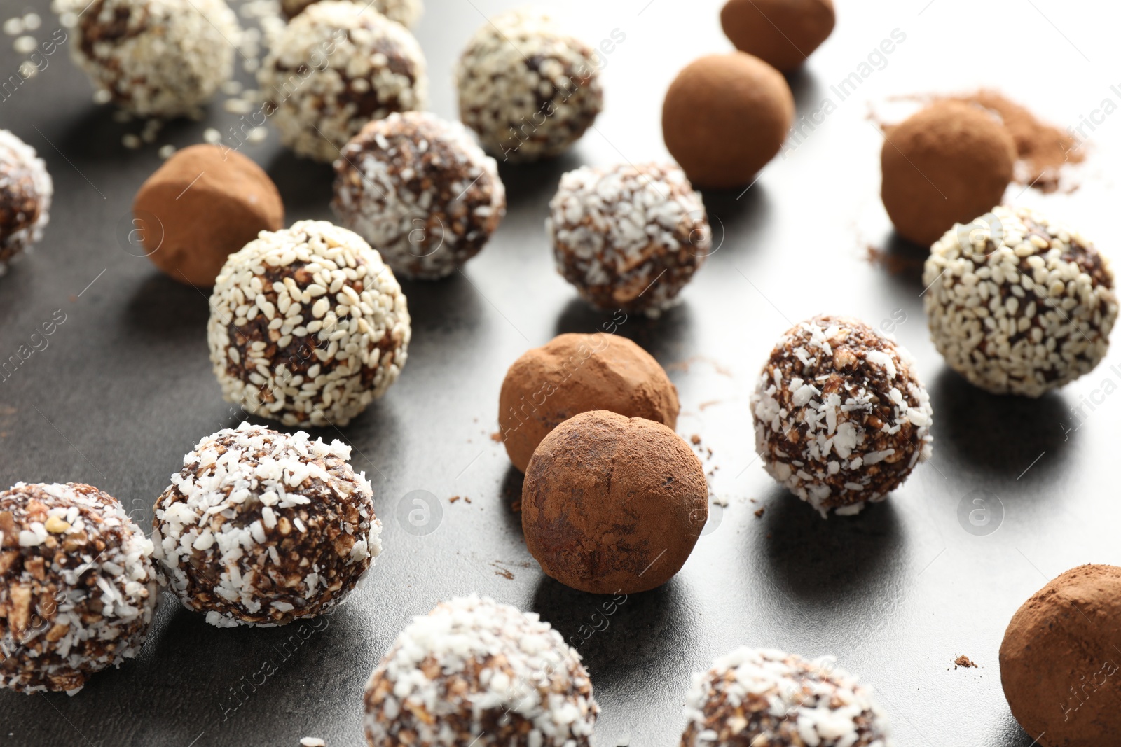 Tasty chocolate candies with cocoa powder, nuts, coconut flakes and sesame seeds on grey table, closeup Photo of Tasty chocolate candies with cocoa powder, nuts, coconut flakes and sesame seeds on grey table, closeup