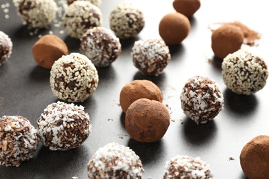 Photo of Tasty chocolate candies with cocoa powder, nuts, coconut flakes and sesame seeds on grey table, closeup