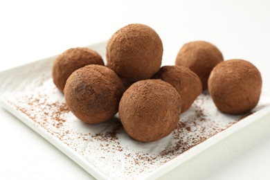 Photo of Tasty chocolate candies with cocoa powder on white table, closeup