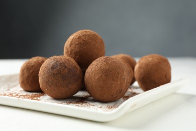 Photo of Tasty chocolate candies with cocoa powder on white table, closeup