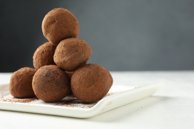 Photo of Tasty chocolate candies with cocoa powder on white table, closeup. Space for text
