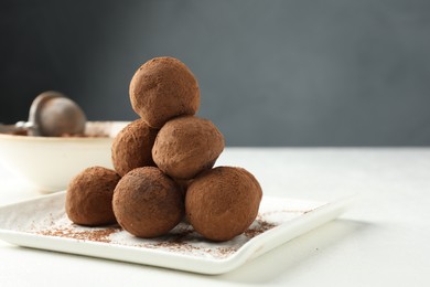Photo of Tasty chocolate candies with cocoa powder on white table, closeup. Space for text