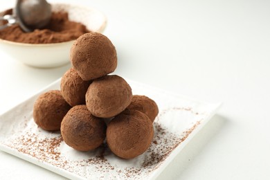 Photo of Tasty chocolate candies with cocoa powder on white table, closeup. Space for text