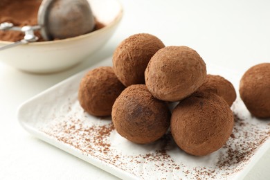 Photo of Tasty chocolate candies with cocoa powder on white table, closeup