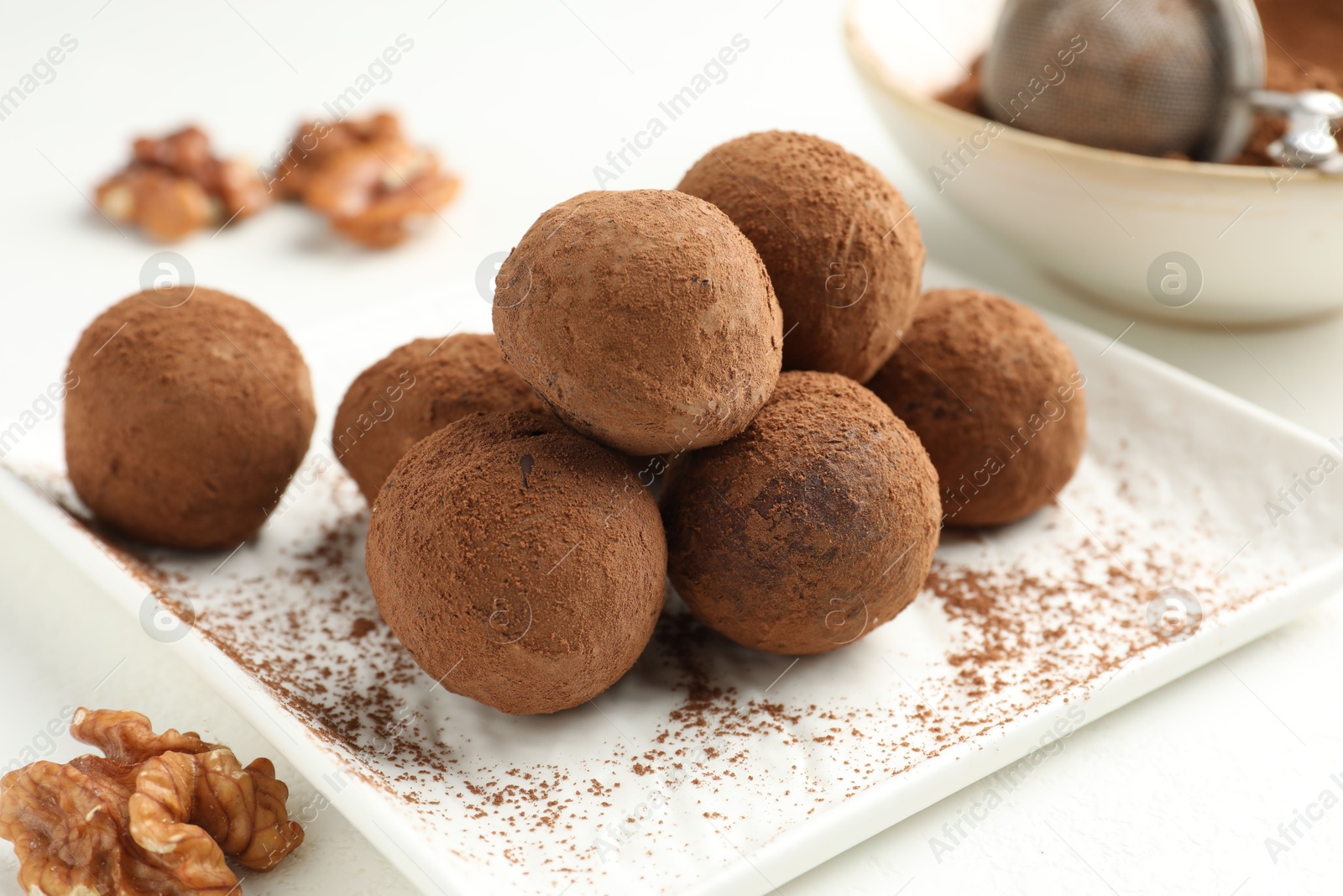 Tasty chocolate candies with cocoa powder and walnuts on white table, closeup Photo of Tasty chocolate candies with cocoa powder and walnuts on white table, closeup