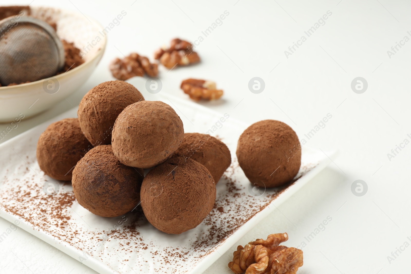 Tasty chocolate candies with cocoa powder and walnuts on white table, closeup Photo of Tasty chocolate candies with cocoa powder and walnuts on white table, closeup