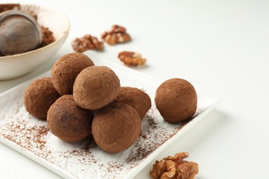 Photo of Tasty chocolate candies with cocoa powder and walnuts on white table, closeup