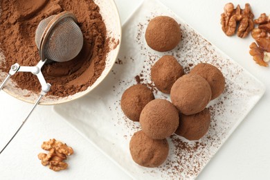Photo of Tasty chocolate candies with cocoa powder and walnuts on white table, flat lay