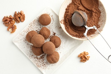 Photo of Tasty chocolate candies with cocoa powder and walnuts on white table, flat lay