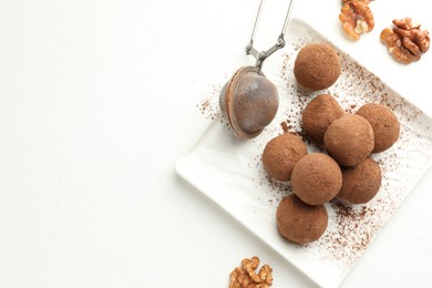 Photo of Tasty chocolate candies with cocoa powder and walnuts on white table, flat lay. Space for text