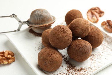 Photo of Tasty chocolate candies with cocoa powder and walnuts on white table, closeup