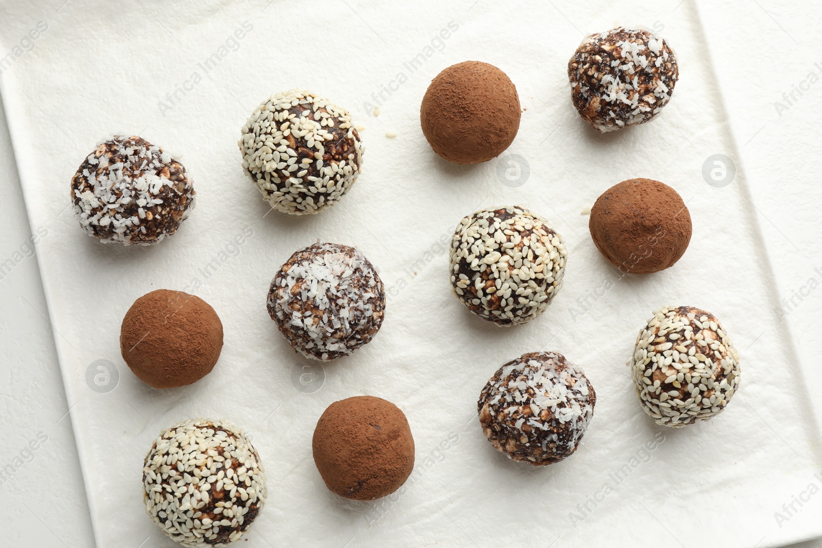 Tasty chocolate candies with cocoa powder, nuts and sesame seeds on white table, top view Photo of Tasty chocolate candies with cocoa powder, nuts and sesame seeds on white table, top view