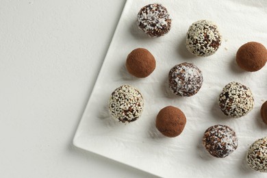 Photo of Tasty chocolate candies with cocoa powder, nuts and sesame seeds on white table, top view. Space for text