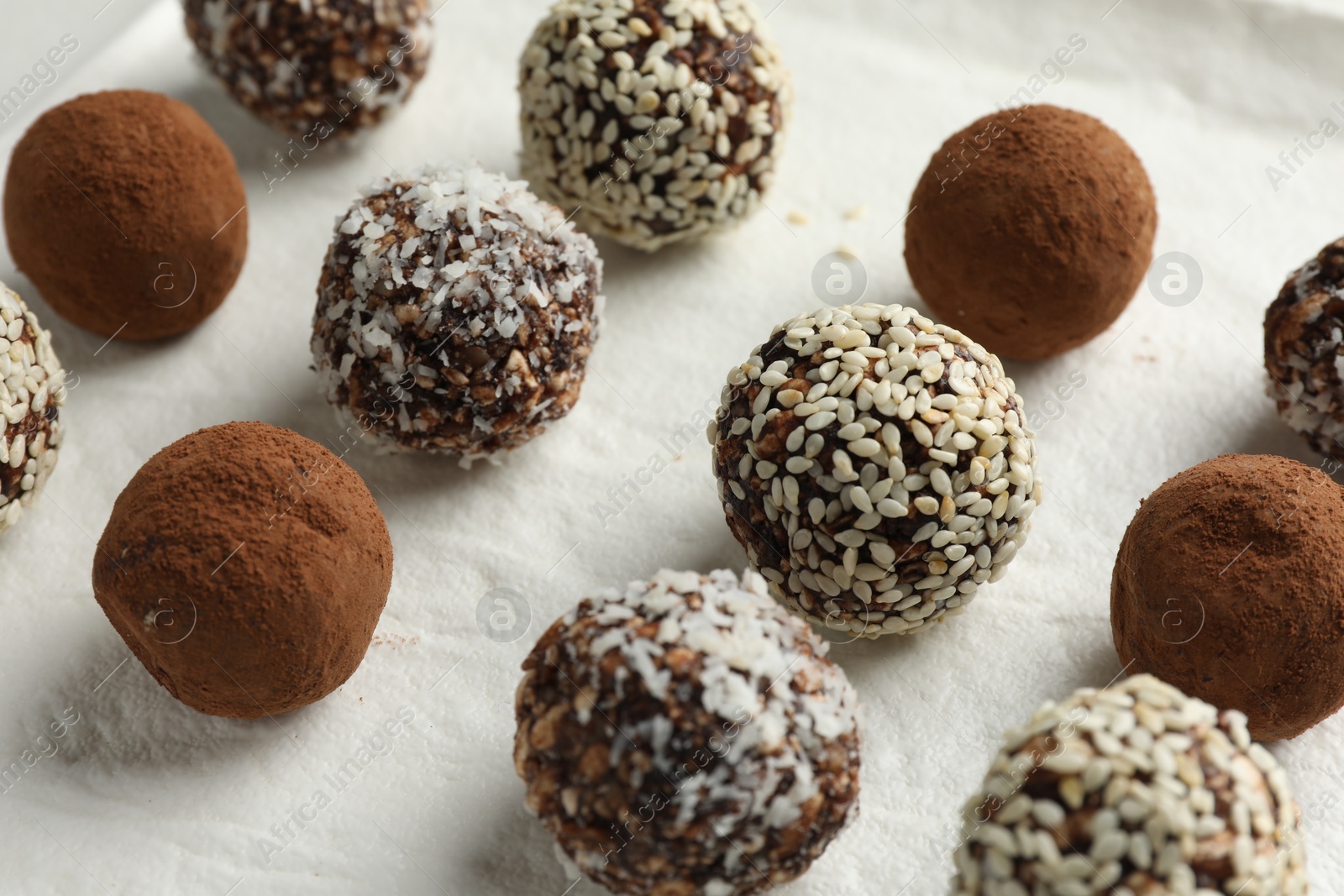 Tasty chocolate candies with cocoa powder, nuts and sesame seeds on white board, closeup Photo of Tasty chocolate candies with cocoa powder, nuts and sesame seeds on white board, closeup