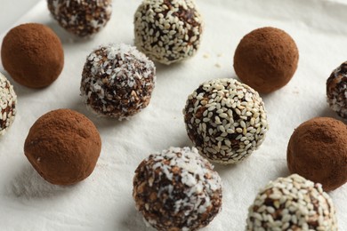 Photo of Tasty chocolate candies with cocoa powder, nuts and sesame seeds on white board, closeup