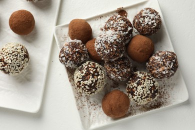 Photo of Tasty chocolate candies with cocoa powder, nuts and sesame seeds on white table, flat lay