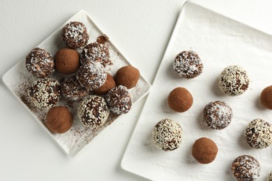Photo of Tasty chocolate candies with cocoa powder, nuts and sesame seeds on white table, flat lay