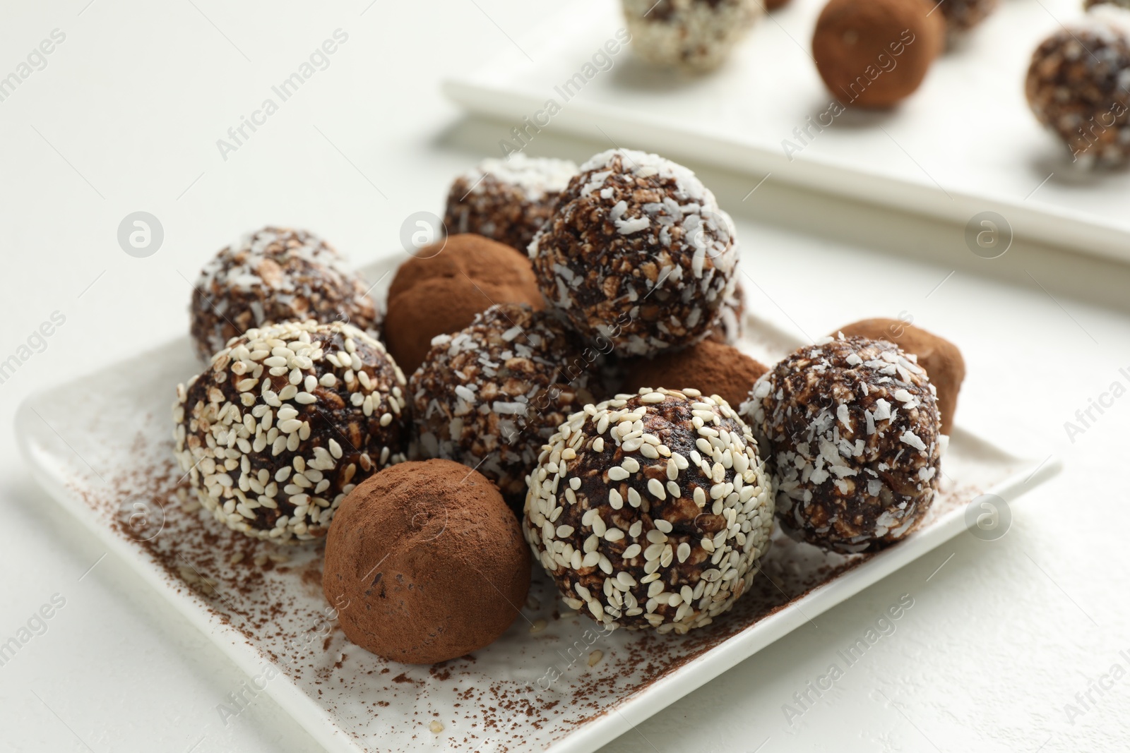 Tasty chocolate candies with cocoa powder, nuts and sesame seeds on white table, closeup Photo of Tasty chocolate candies with cocoa powder, nuts and sesame seeds on white table, closeup