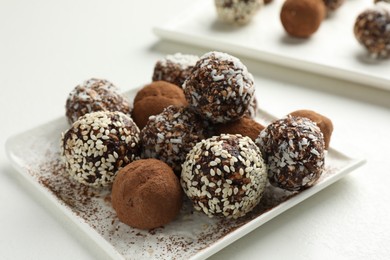 Photo of Tasty chocolate candies with cocoa powder, nuts and sesame seeds on white table, closeup