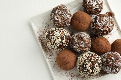 Photo of Tasty chocolate candies with cocoa powder, nuts and sesame seeds on white table, top view. Space for text