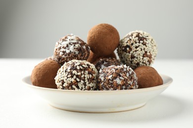 Photo of Tasty chocolate candies with cocoa powder, nuts and sesame seeds on white table, closeup