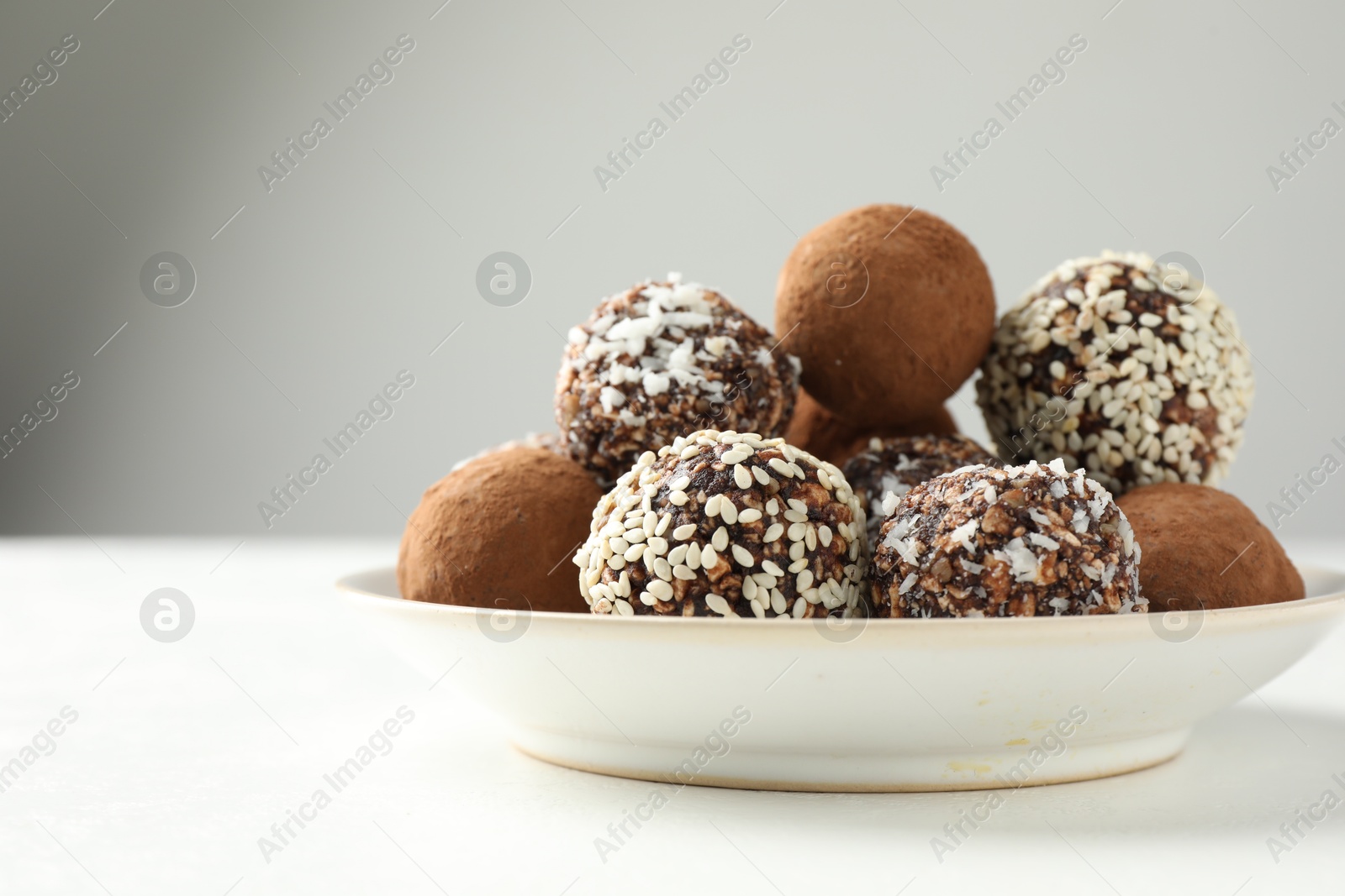 Tasty chocolate candies with cocoa powder, nuts and sesame seeds on white table, closeup Photo of Tasty chocolate candies with cocoa powder, nuts and sesame seeds on white table, closeup