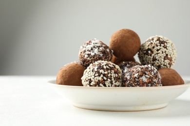 Photo of Tasty chocolate candies with cocoa powder, nuts and sesame seeds on white table, closeup