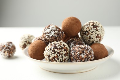 Photo of Tasty chocolate candies with cocoa powder, nuts and sesame seeds on white table, closeup