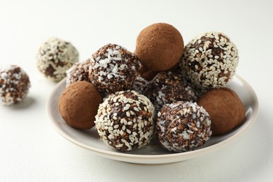 Photo of Tasty chocolate candies with cocoa powder, nuts and sesame seeds on white table, closeup