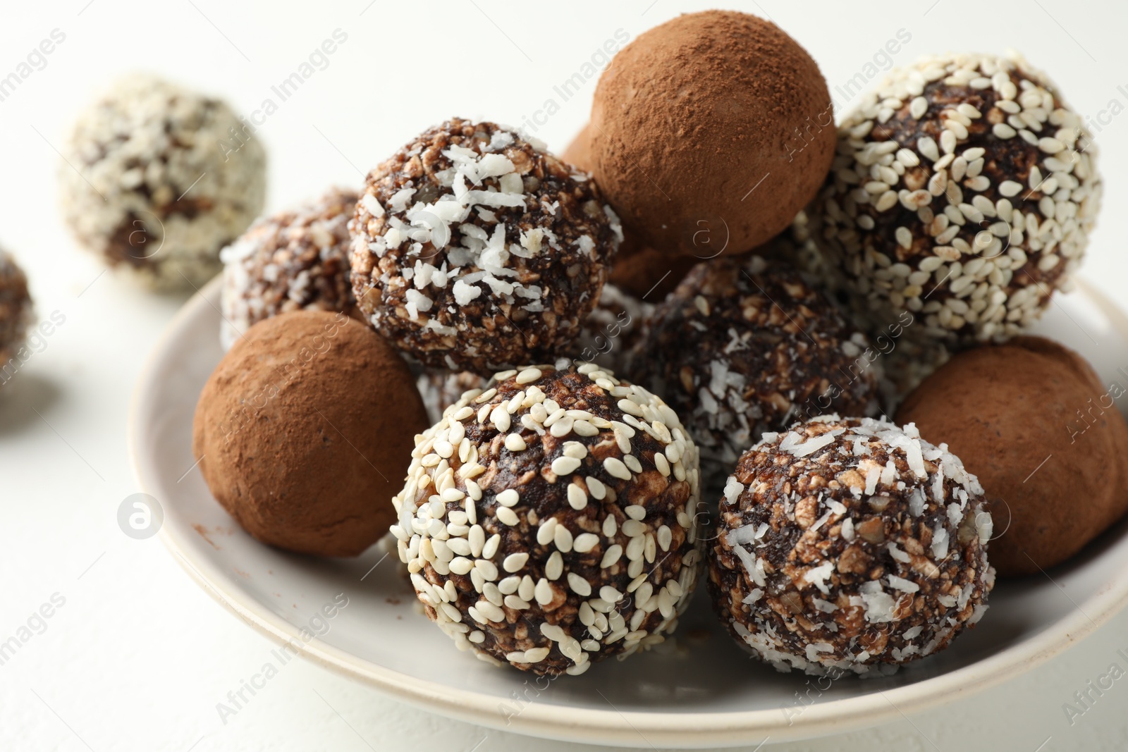Tasty chocolate candies with cocoa powder, nuts and sesame seeds on white table, closeup Photo of Tasty chocolate candies with cocoa powder, nuts and sesame seeds on white table, closeup