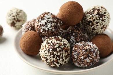 Photo of Tasty chocolate candies with cocoa powder, nuts and sesame seeds on white table, closeup