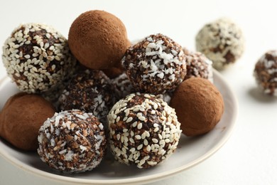 Photo of Tasty chocolate candies with cocoa powder, nuts and sesame seeds on white table, closeup