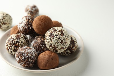 Photo of Tasty chocolate candies with cocoa powder, nuts and sesame seeds on white table, closeup. Space for text