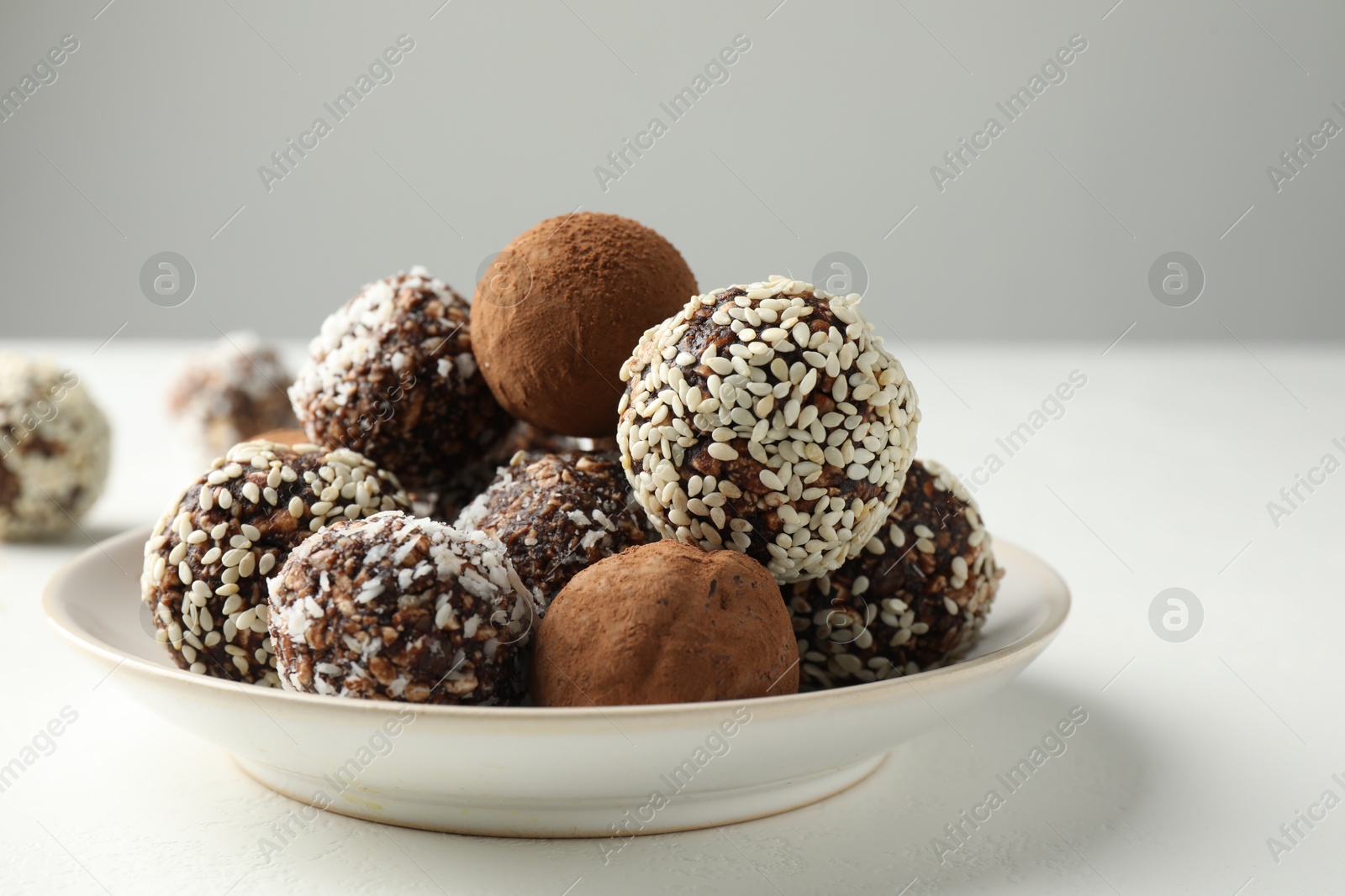 Tasty chocolate candies with cocoa powder, nuts and sesame seeds on white table, closeup Photo of Tasty chocolate candies with cocoa powder, nuts and sesame seeds on white table, closeup