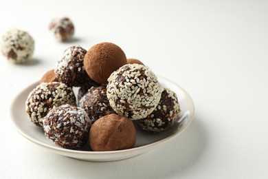 Photo of Tasty chocolate candies with cocoa powder, nuts and sesame seeds on white table, closeup. Space for text