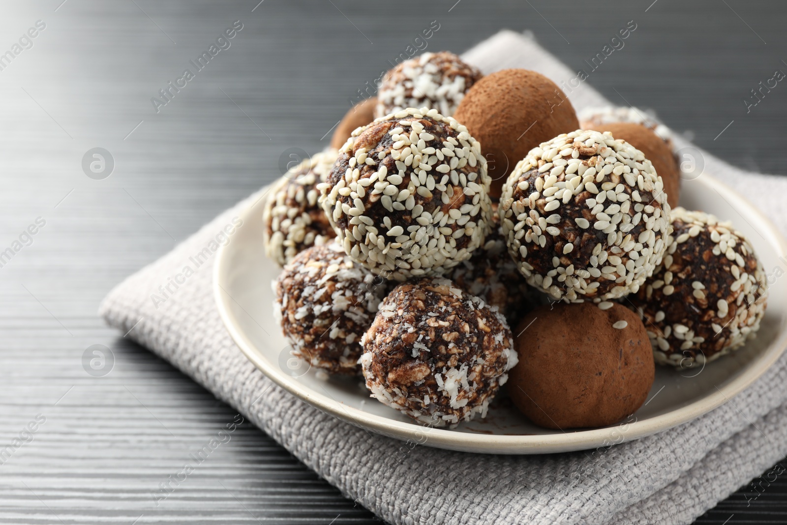 Tasty chocolate candies with cocoa powder, nuts and sesame seeds on black textured table, closeup Photo of Tasty chocolate candies with cocoa powder, nuts and sesame seeds on black textured table, closeup