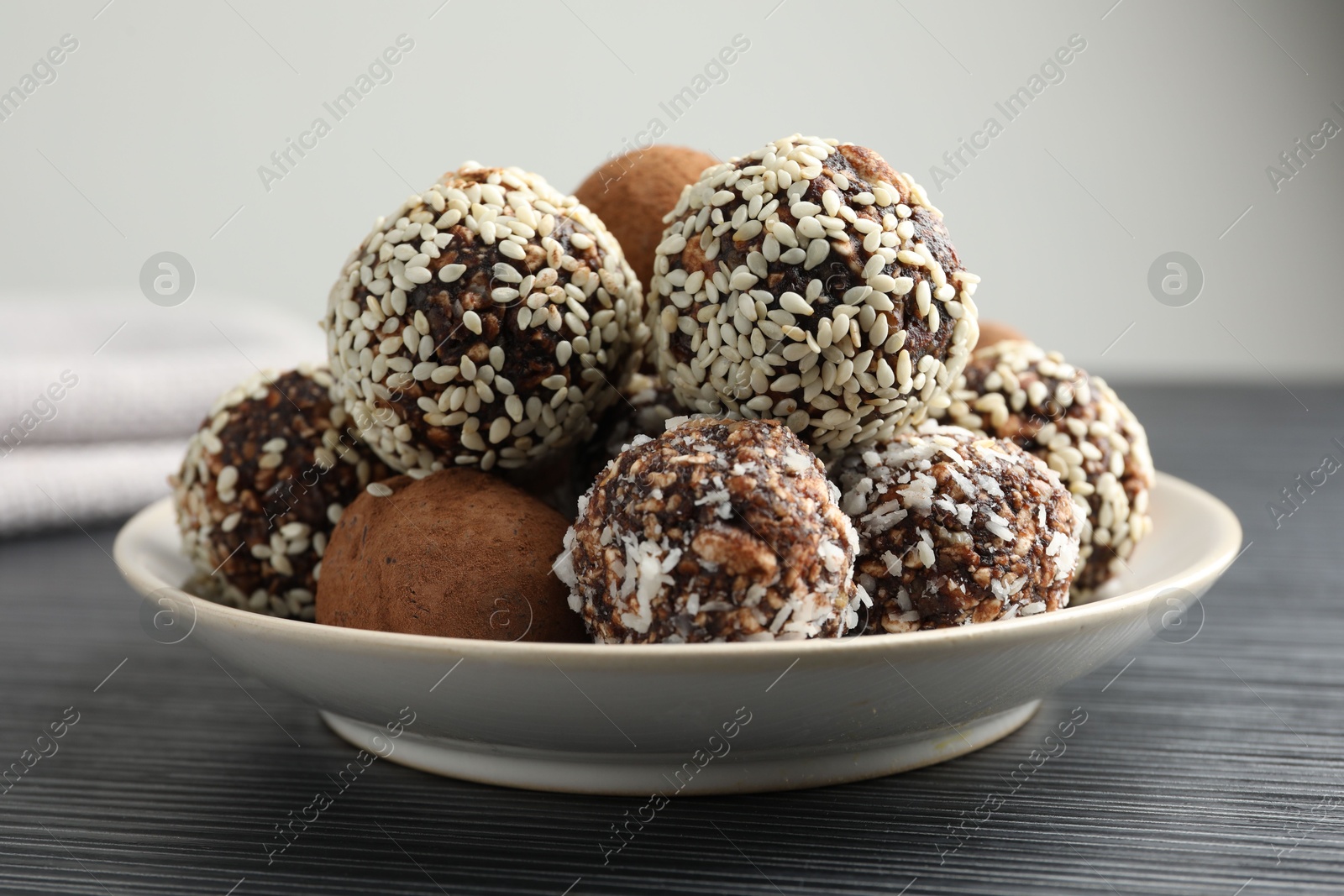 Tasty chocolate candies with cocoa powder, nuts and sesame seeds on black textured table, closeup Photo of Tasty chocolate candies with cocoa powder, nuts and sesame seeds on black textured table, closeup