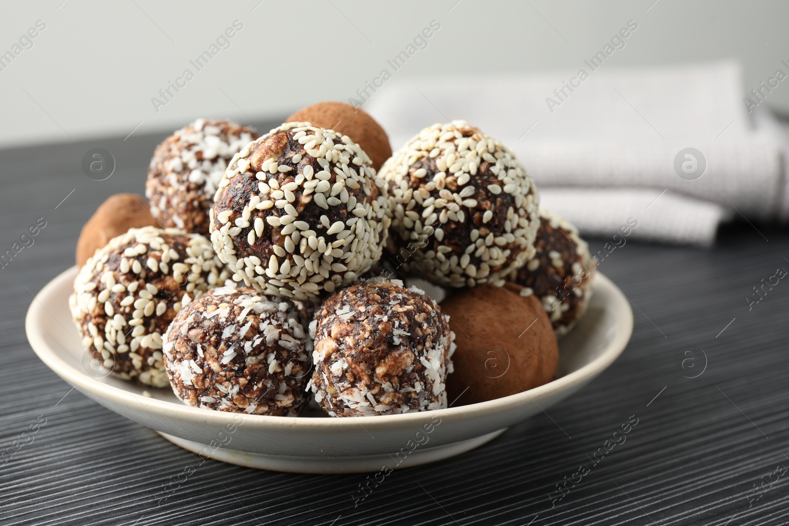 Tasty chocolate candies with cocoa powder, nuts and sesame seeds on black textured table, closeup Photo of Tasty chocolate candies with cocoa powder, nuts and sesame seeds on black textured table, closeup
