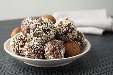 Photo of Tasty chocolate candies with cocoa powder, nuts and sesame seeds on black textured table, closeup