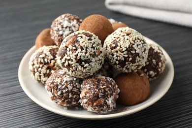 Photo of Tasty chocolate candies with cocoa powder, nuts and sesame seeds on black textured table, closeup