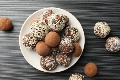 Photo of Tasty chocolate candies with cocoa powder, nuts and sesame seeds on black textured table, flat lay