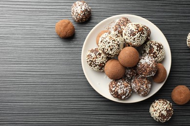 Photo of Tasty chocolate candies with cocoa powder, nuts and sesame seeds on black textured table, flat lay. Space for text