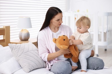 Photo of Mother with her cute little baby and toy on bed in room