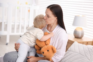 Photo of Mother with her cute little baby and toy on bed in room
