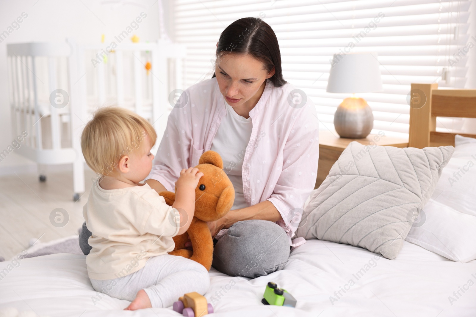 Mother with her cute little baby and toy on bed in room Photo of Mother with her cute little baby and toy on bed in room