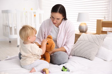 Photo of Mother with her cute little baby and toy on bed in room