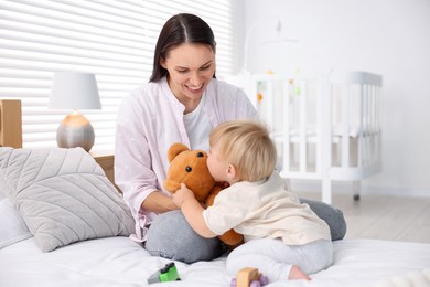 Photo of Mother with her cute little baby and toy on bed in room